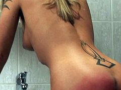 Seductive blond whore with tattoos all over her appetizing body stands naked by the sink with her juicy ass all red from hard slapping.