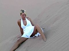 Sweet blonde babe in a white dress makes a solo show in the heart of a desert. She lies down on the sand. Her dress is flutters so that you can see her ass and pussy.