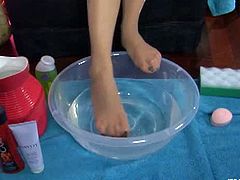 Jenny F. soaks her feet in a basin with water. She still has pantyhose on, but she starts washing her feet with them on. Then, she uses a towel to dry herself up.