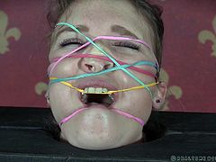 Ashley is tightly wedged in a single-board version of stocks. The topless beauty now has rubber bands stretched all over her face. She doesn't want one of those things to snap against her, so she keeps still, until the cattle prod zips her a little.